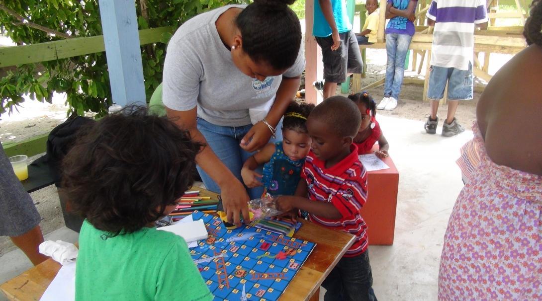 Two young children get help with an activity during class at their kindergarten from a Projects Abroad volunteer in Belize. A volunteer with children in Belize helps two young students with an educational activity at a kindergarten.